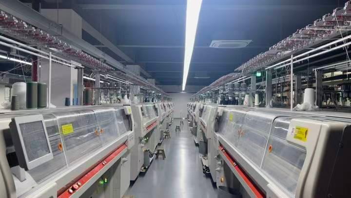 Parallel rows of computerized knitting equipment with yarn feeds above the machines
