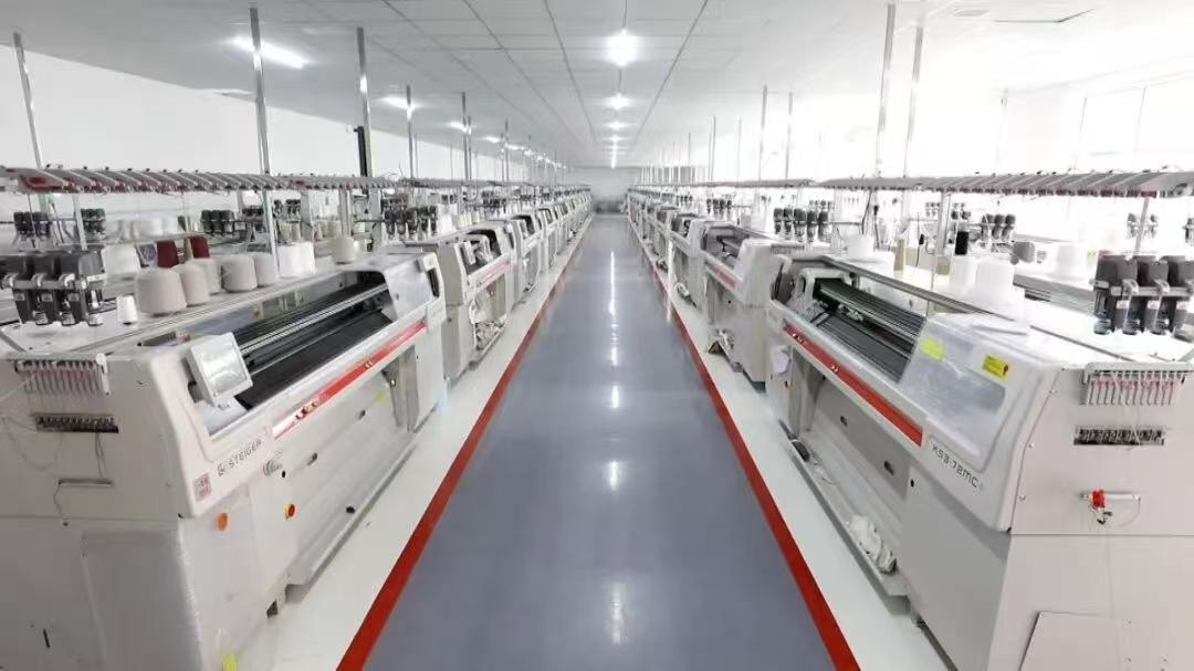 A bright knitting workshop with production machines arranged along a central aisle