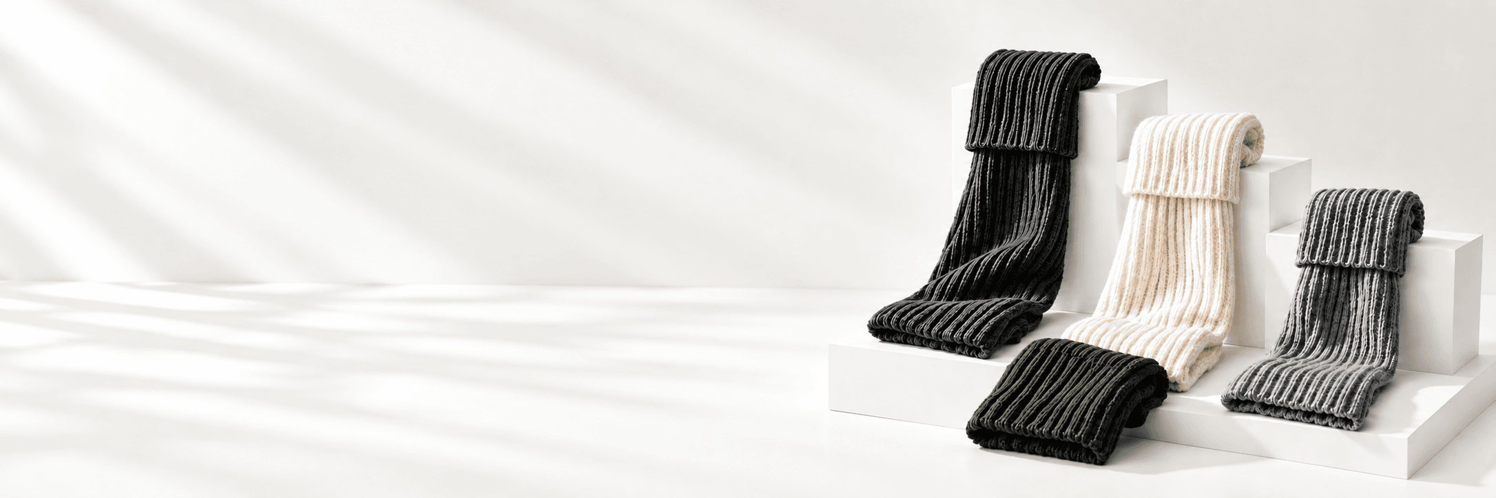 Ivory, charcoal and gray rib-knit leg warmers arranged on white studio plinths